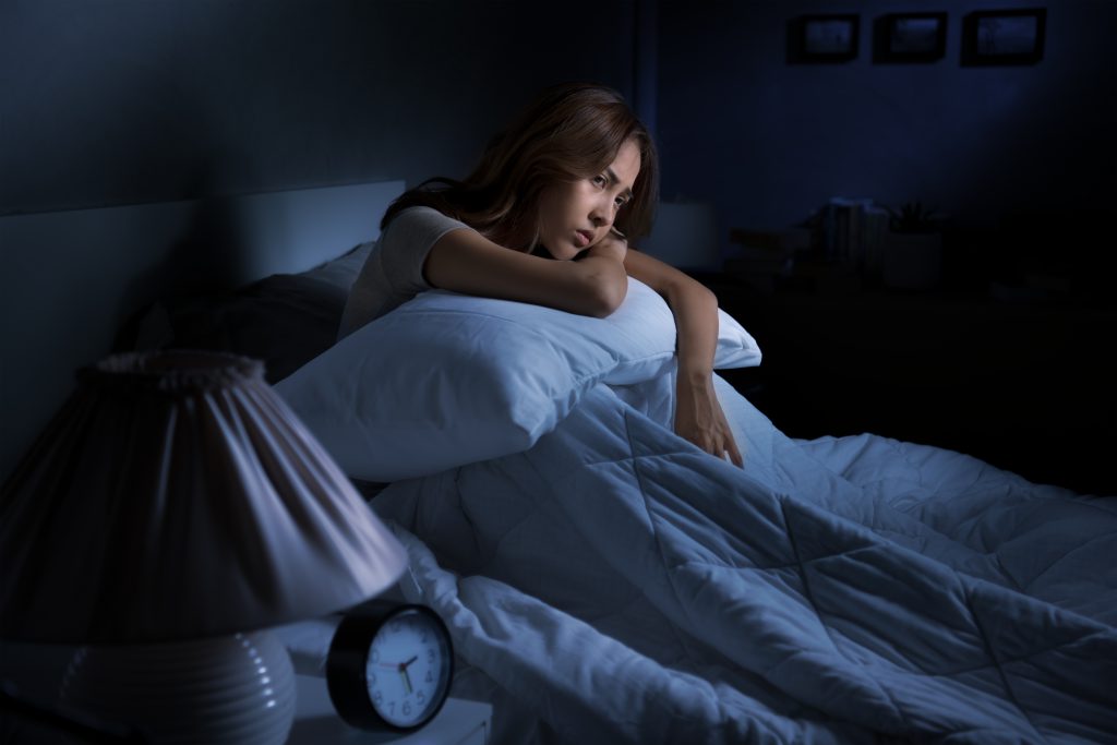 Depressed young Asian woman sitting in bed cannot sleep from insomnia